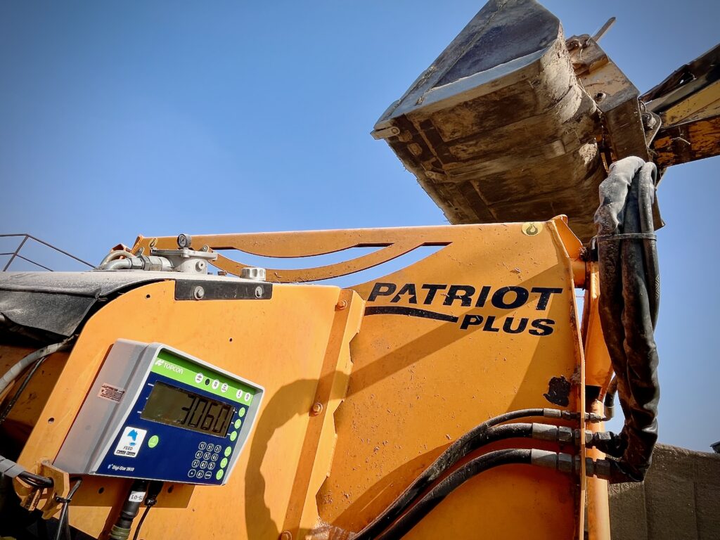 Pohled z podhledu na oranžový zemědělský stroj s nápisem „PATRIOT PLUS“.
